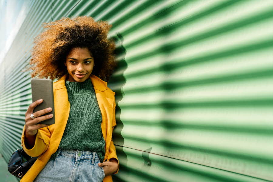 Jente med mobil foran grønn vegg