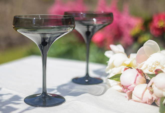 To Noir cocktailglass fra Magnor som står på et bord ute ved siden av en bukett
