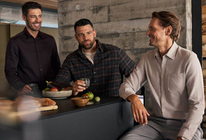 Tre menn som sitter rundt en frokostbar med mat og drikke på bordet