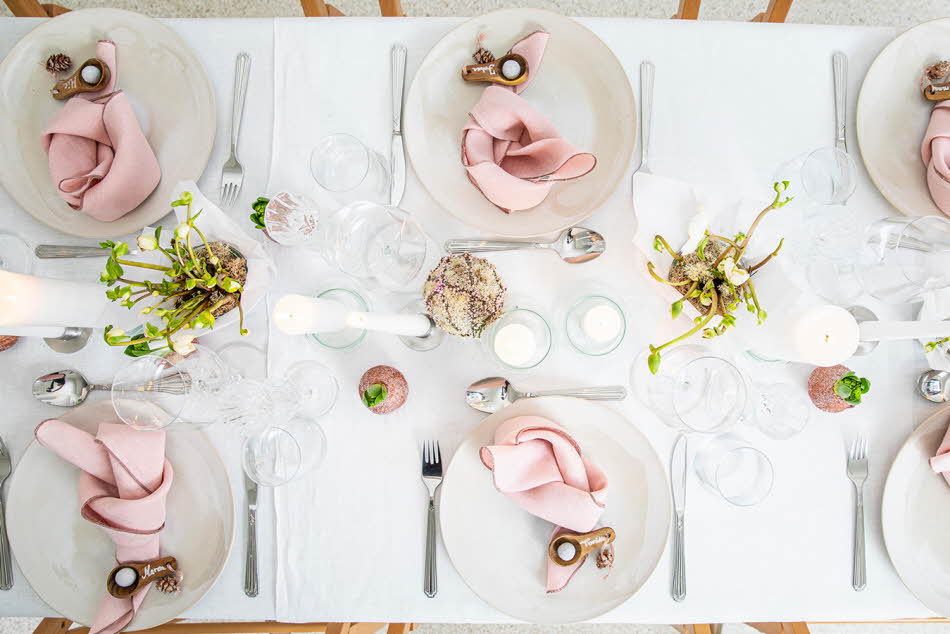 Langbord dekker til gjester med rosa servietter og grønn naturlig dekorasjon