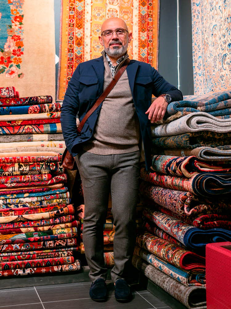 mann i brungrå dressbukse, beige genser og blå jakke, brun veske og mørke sko