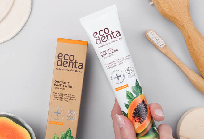 En hånd som holder en tube med Eco Denta tannkrem, ved siden av boksen den var i og en tannbørste