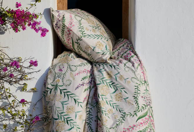 En dyne og pute med blomstrete sengesett henger ut av et vindu