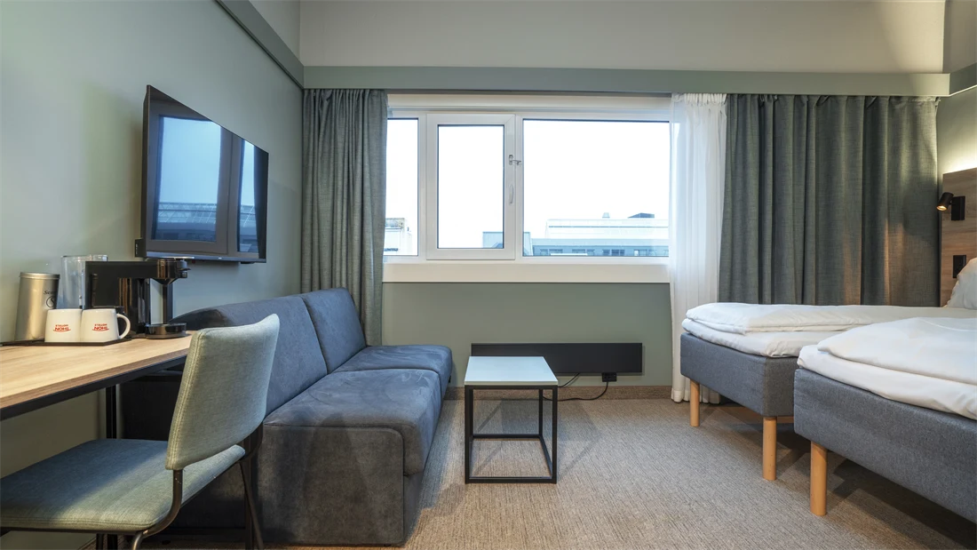 Sofa, TV, skrivebord og to enkeltsenger i Standard Twin Room hos Thon Partner Hotel Kristiansand.