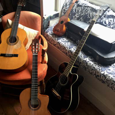 Fire gitarer i forskjellige størrelser ligger i stol ved siden av et piano