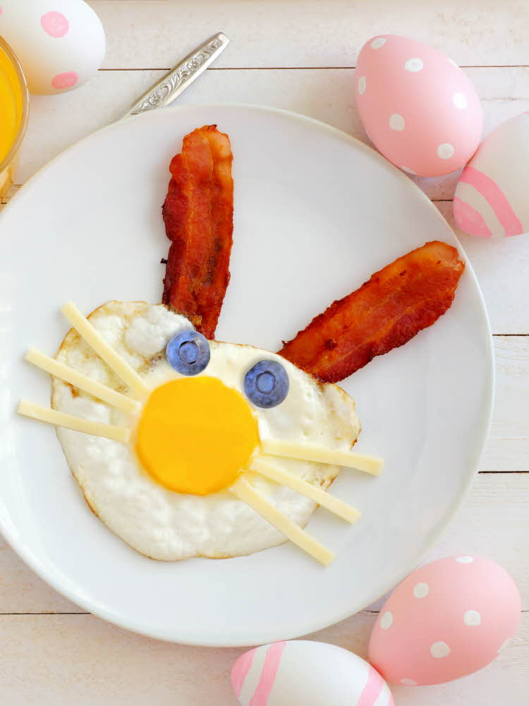 Speilegg med bacon formet som en kanin Bord dekket med egg i pastellfarger
