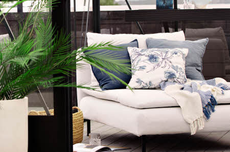 sofastol med blå og lyse puter, blått og hvitt pledd og en grønn palme i en stor, lys potte.