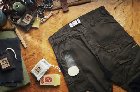 En Fjallraven-bukse med et voksstykke oppå, mye voksutstyr ved siden av og over buksen