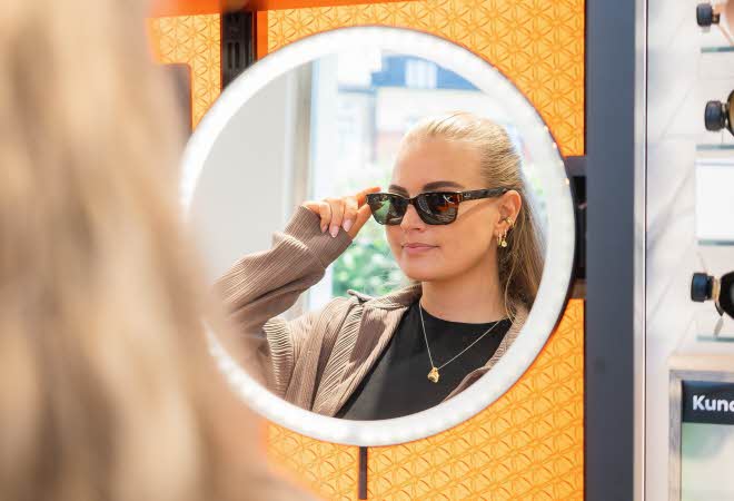 En kvinne ser seg i speilet iført solbriller fra Brilleland