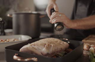 Nærbilde av hendene til en person som krydrer en ribbe som ligger i en form