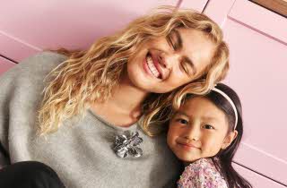 Dame i grå genser med sølvbrosje ved siden av en jente i paljettopp.