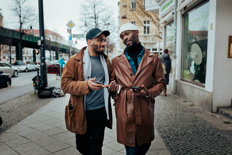 To menn kledd i brune jakker, denim, luer og caps som går i gatene
