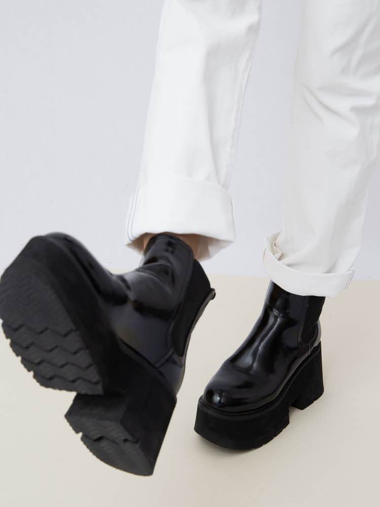  Ben med hvite jeans og svarte boots med kraftig såle innendørs på hvit bakgrunn.