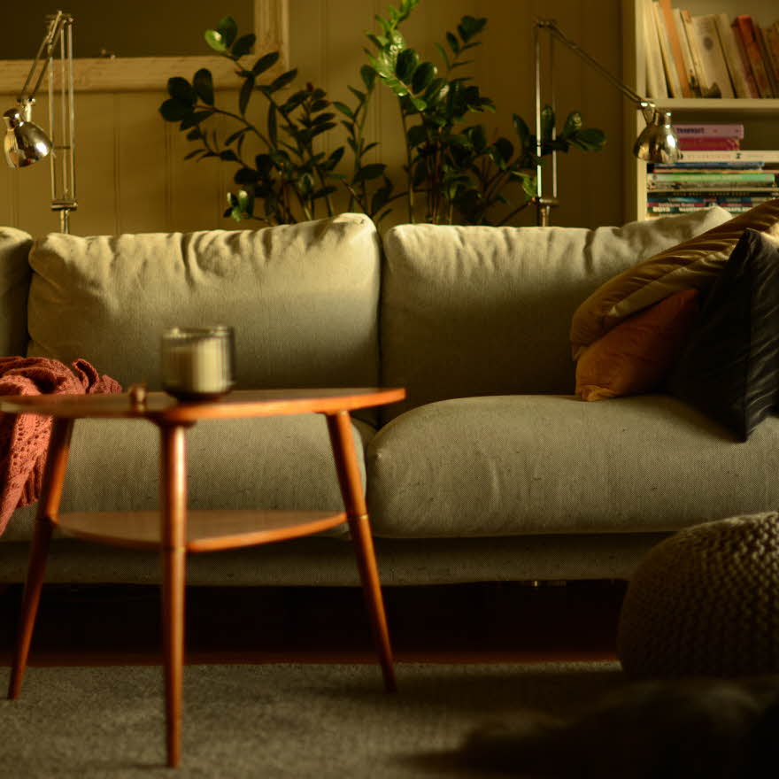 Stue med lun atmosfære og sofa med puter i høstlige farger og trebord med stearinlys i front