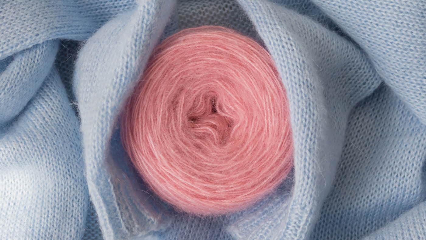 Blå genser ligger rundt rosa garnnøste