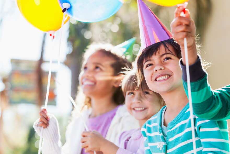 Tre barn som smiler med ballonger i hendene