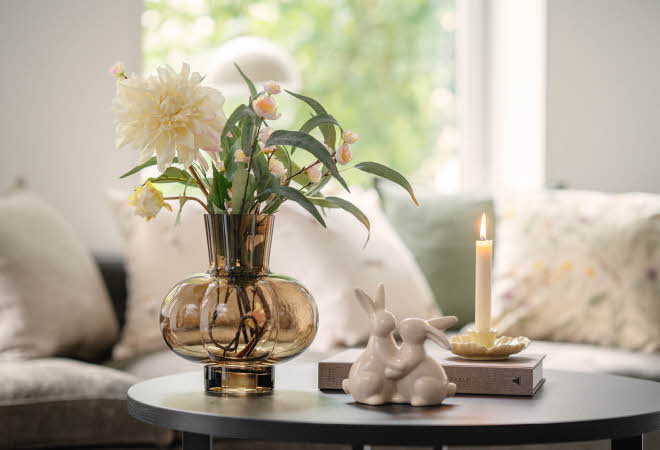 Rundt bord med vase med blomster, tent lys og keramiske kaninfigurer.