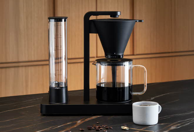 Moderne kaffetrakter med glasskanne og kopp på benk.