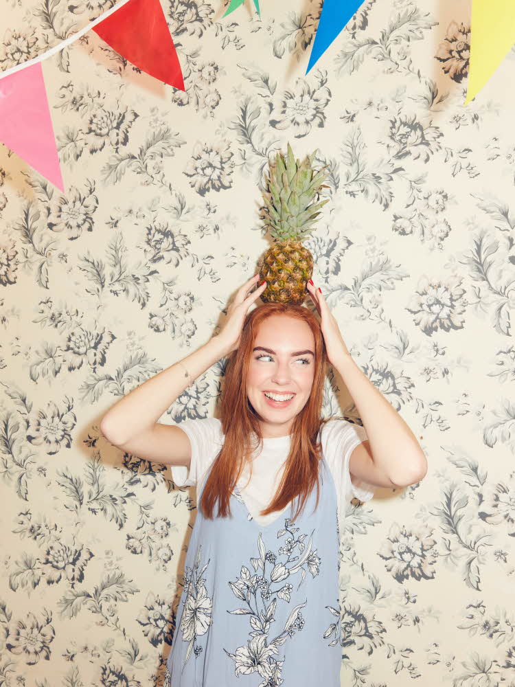 Jente som balanserer en ananas på hodet Bord med forskjellige dekoarsjoner til hawaiifest Bord pyntet til sommerfest med frukt og sterke farger