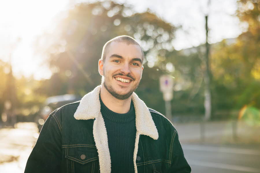 Mann med foret olajakke med pelskrage smiler utendørs 