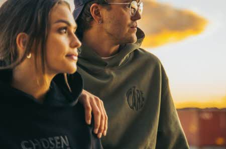 En mann og en kvinne ser på solnedgangen iført gensere fra Chosen