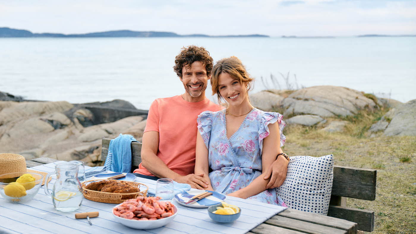 En mann og en kvinne sitter ved et bord ute ved vannet med reker på bordet