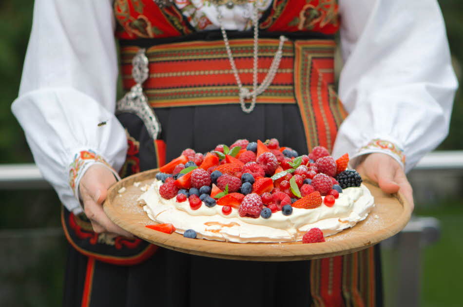 Dame i bunad holder et kakefat med Pavlova fylt med krem og bær
