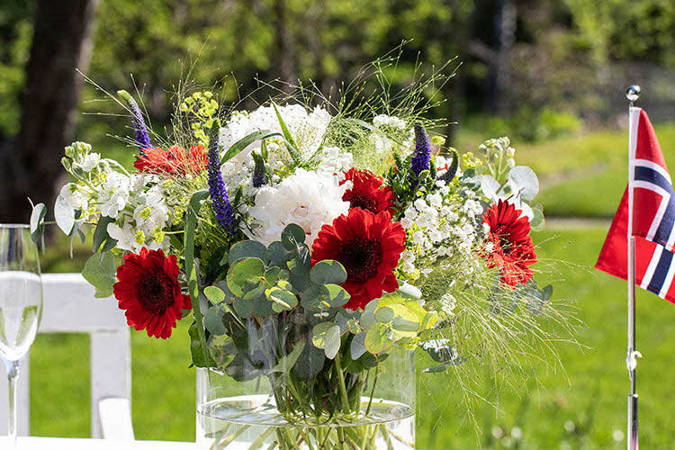 Blomsterbukett og flagg på bord ute med grønt gress i bakgrunnen.