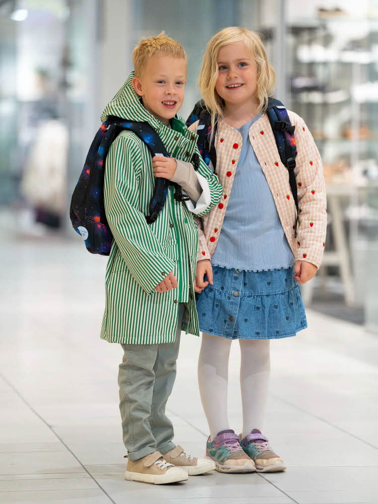 Gutt og jente står ved siden av hverandre på et kjøpesenter med yttertøy og skolesekker