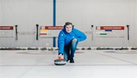 Mann som holder curling-stein på isen i en curlinghall. 