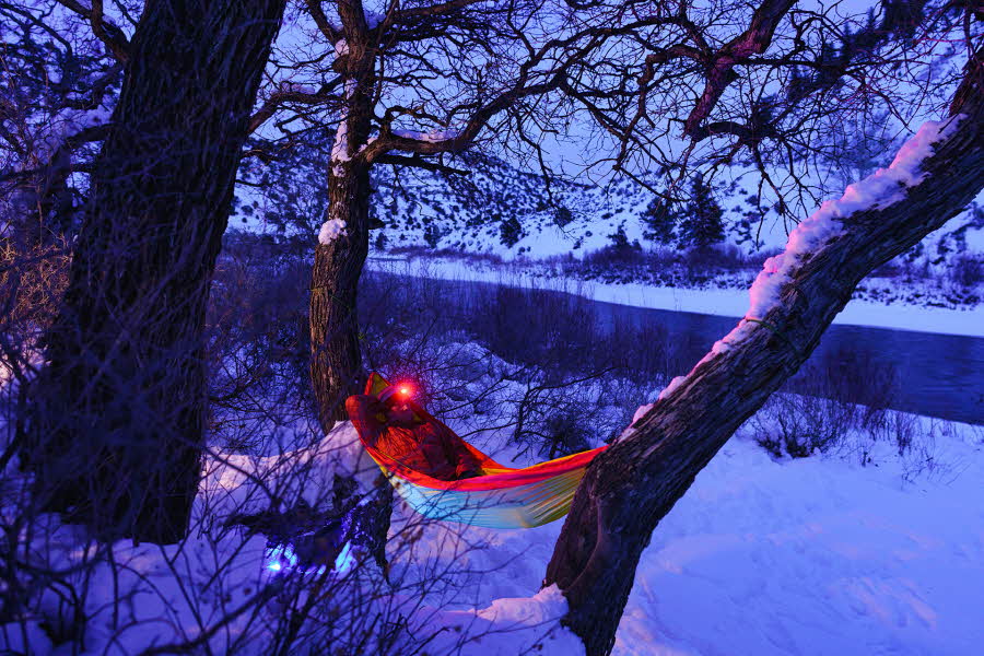 Person med hodelykt på hengekøyetur på vinteren, mellom trær i snødekket landskap.