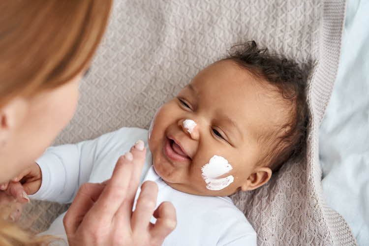 liggende baby som blir smurt på med ansiktskrem av mor