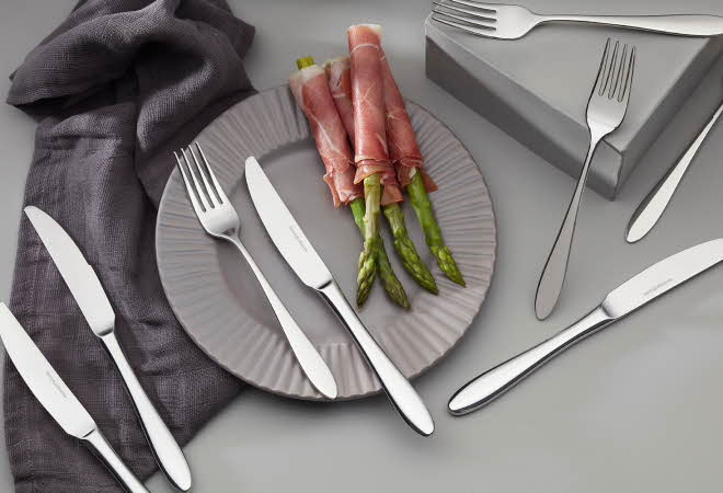 Elegant borddekking med bestikk og tallerken med asparges surret i spekeskinke.