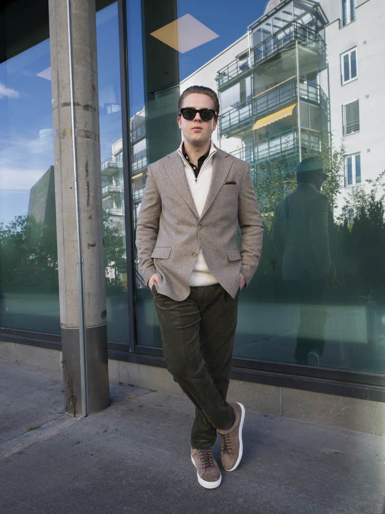 Mann i solbriller, brun blazer, hvit genser, brun bukse og brune sneakers.