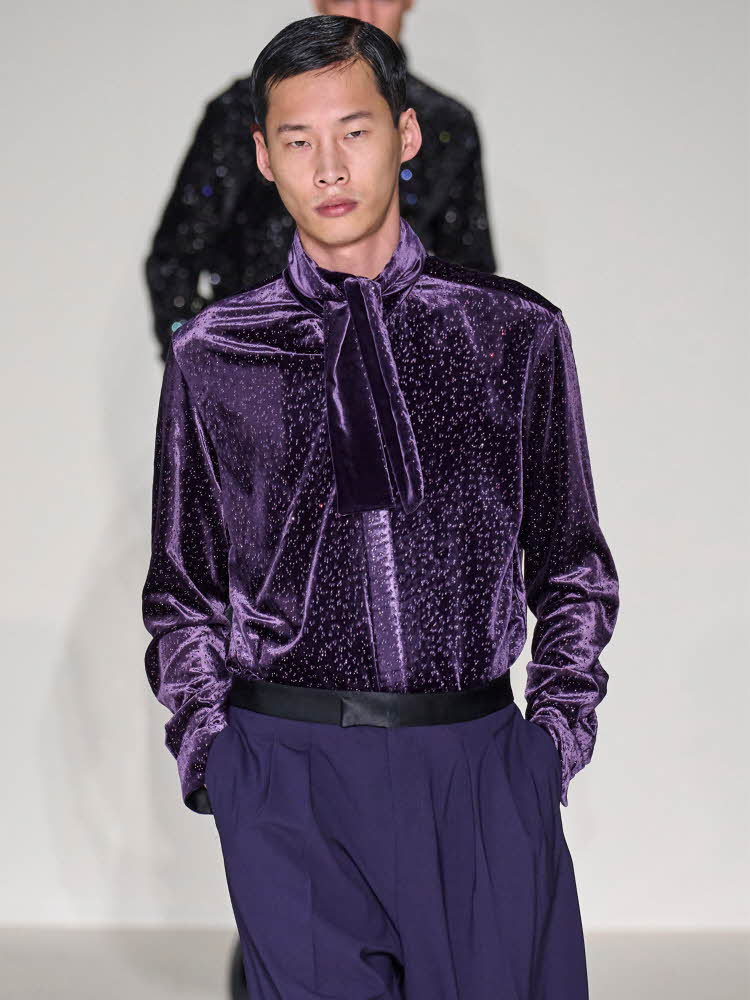 Herremodell på catwalk med lilla skjorte med glitter og lilla bukse.