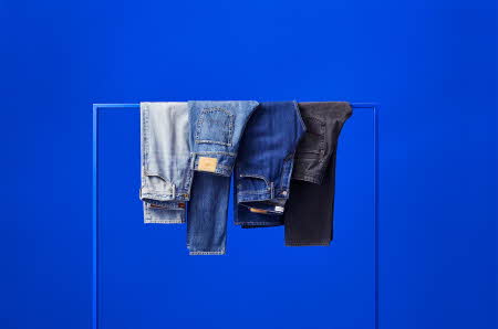jeans i flere farger hengende på et stativ med blå bakgrunn