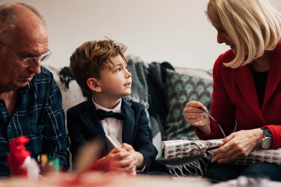 Ung gutt sitter i finstasen mellom sine besteforeldre, hvor bestemor pakker opp julegave