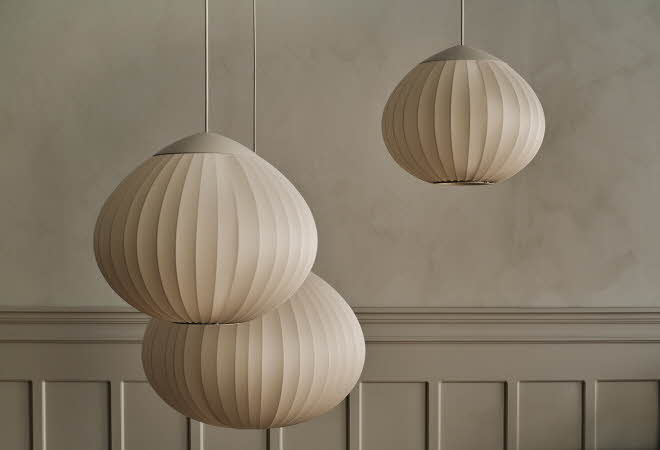 Tre lyse pendellamper med myke former mot en lys vegg.