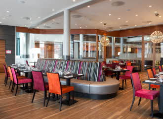 Restaurant med rosa og oransje stoler og detaljer, bord, stoler og sofa.