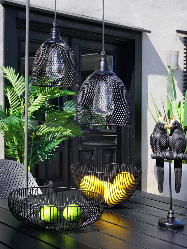 Et spisebord utendørs med pynt i form av lamper, fuglefigur og fruktboller i sort