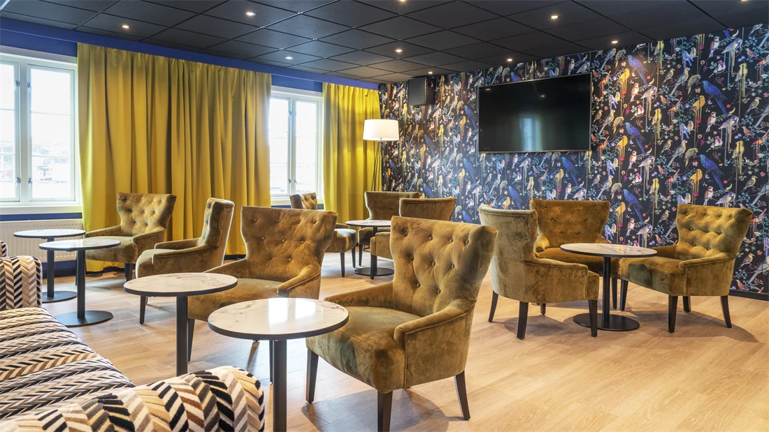 Lounge med sittegrupper, fargerik fugltapet og gule gardiner på Thon Hotel Kristiansund