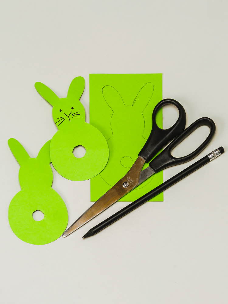 To grønne kaniner, et grønt ark, en blyant og en saks To grønne kaniner av papir og garn