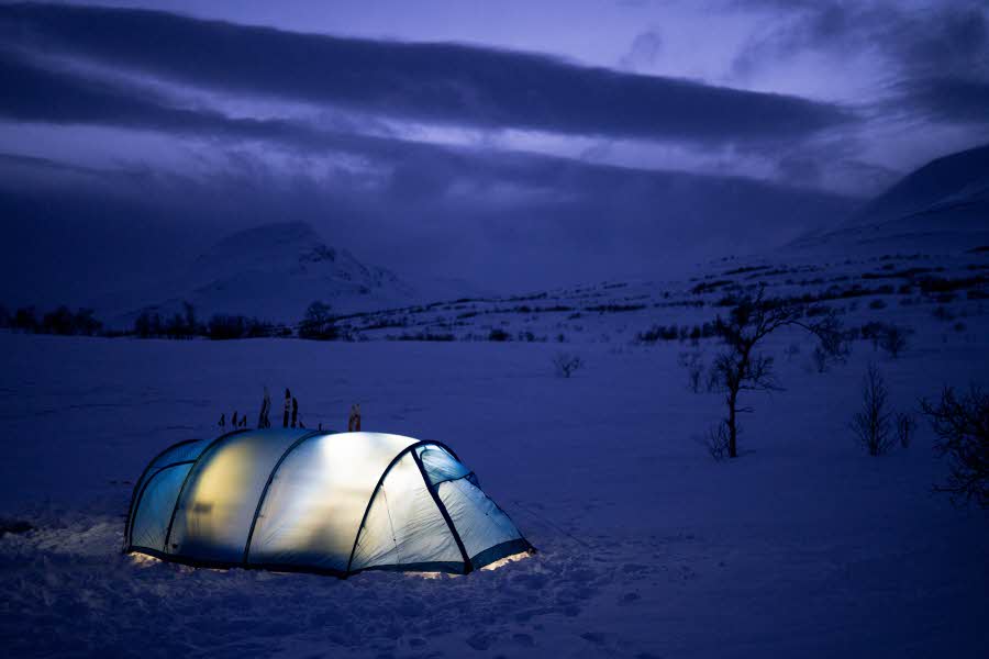 Et telt lyser opp ute i mørk vinternatur