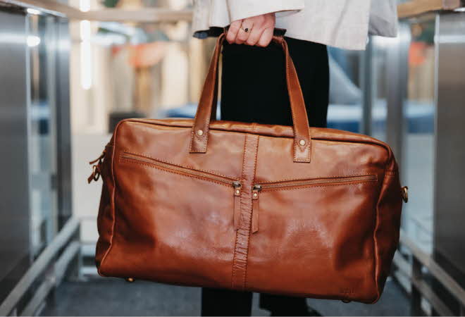 Person som holder en brun skinnbag i et innendørs miljø.