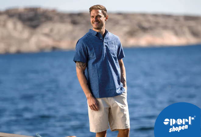 En mann i blå t-skjorte og beige shorts som står foran vannet
