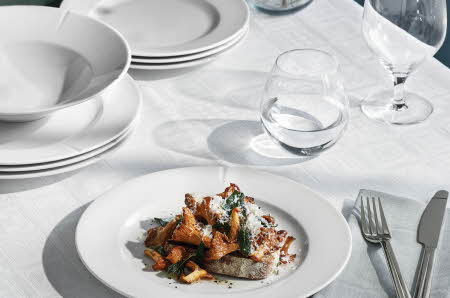 En tallerken med kylling på brød med parmesaen med serviser, glass, vinglass og bestikk liggende rundt på bordet
