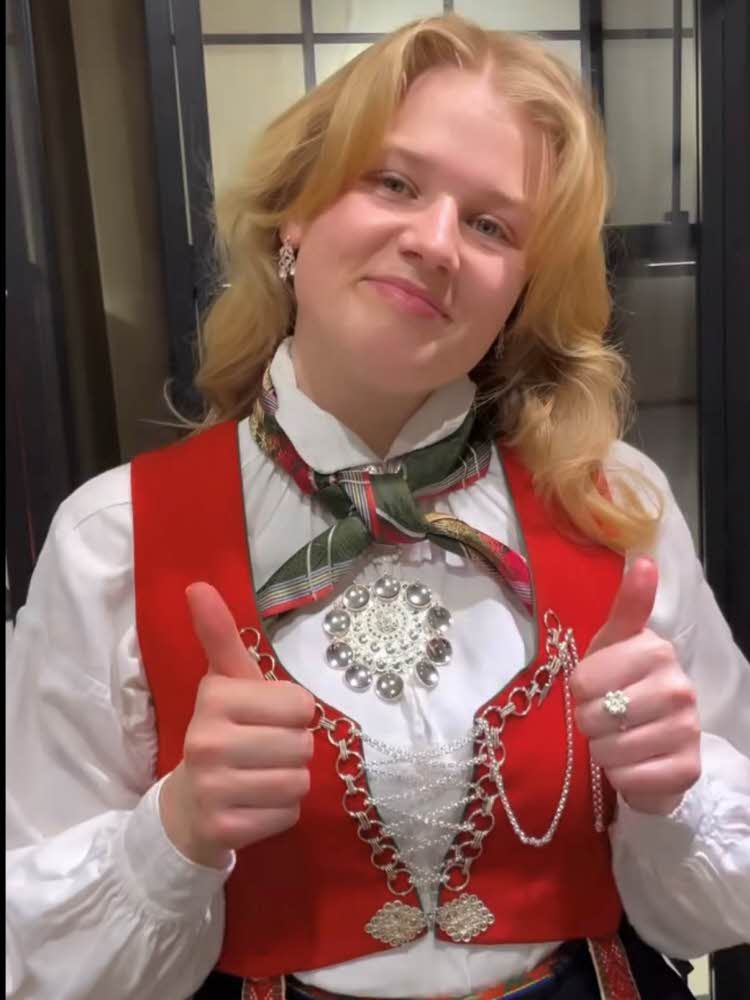 En jente står med bunad pyntet med bunadssølv og skjerf