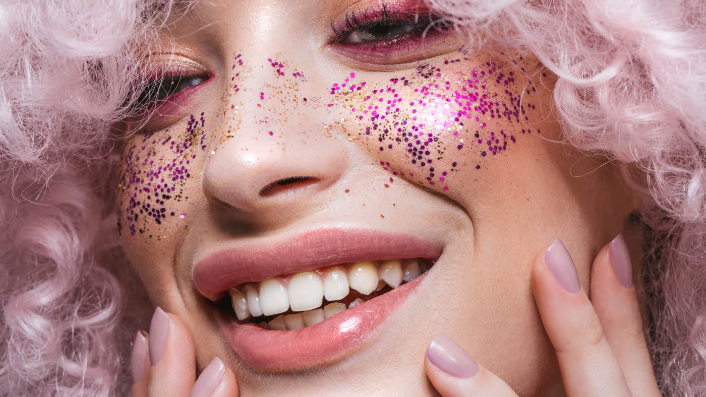 Smilende dame med rosa krøller og rosa glitter i kinnene