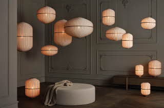 Mørk vegg med mange hengende lamper i varme toner og en rund puff.