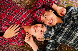 To damer ligger på et teppe iført rutete pysjamas i rødt og blått mønster.